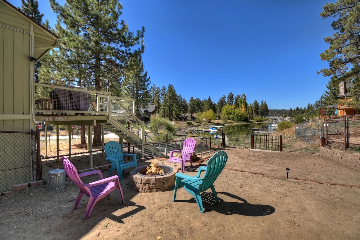 A patio with Adirondack chairs, a fire pit, and a view of a lake and forest.