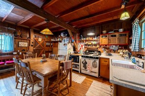 A rustic kitchen with wooden beams, a dining table with chairs, and a variety of kitchen appliances and utensils. - Secluded Mountain Cabin with Creek Near Swallow Falls State Park, West Virginia (Terra Alta)