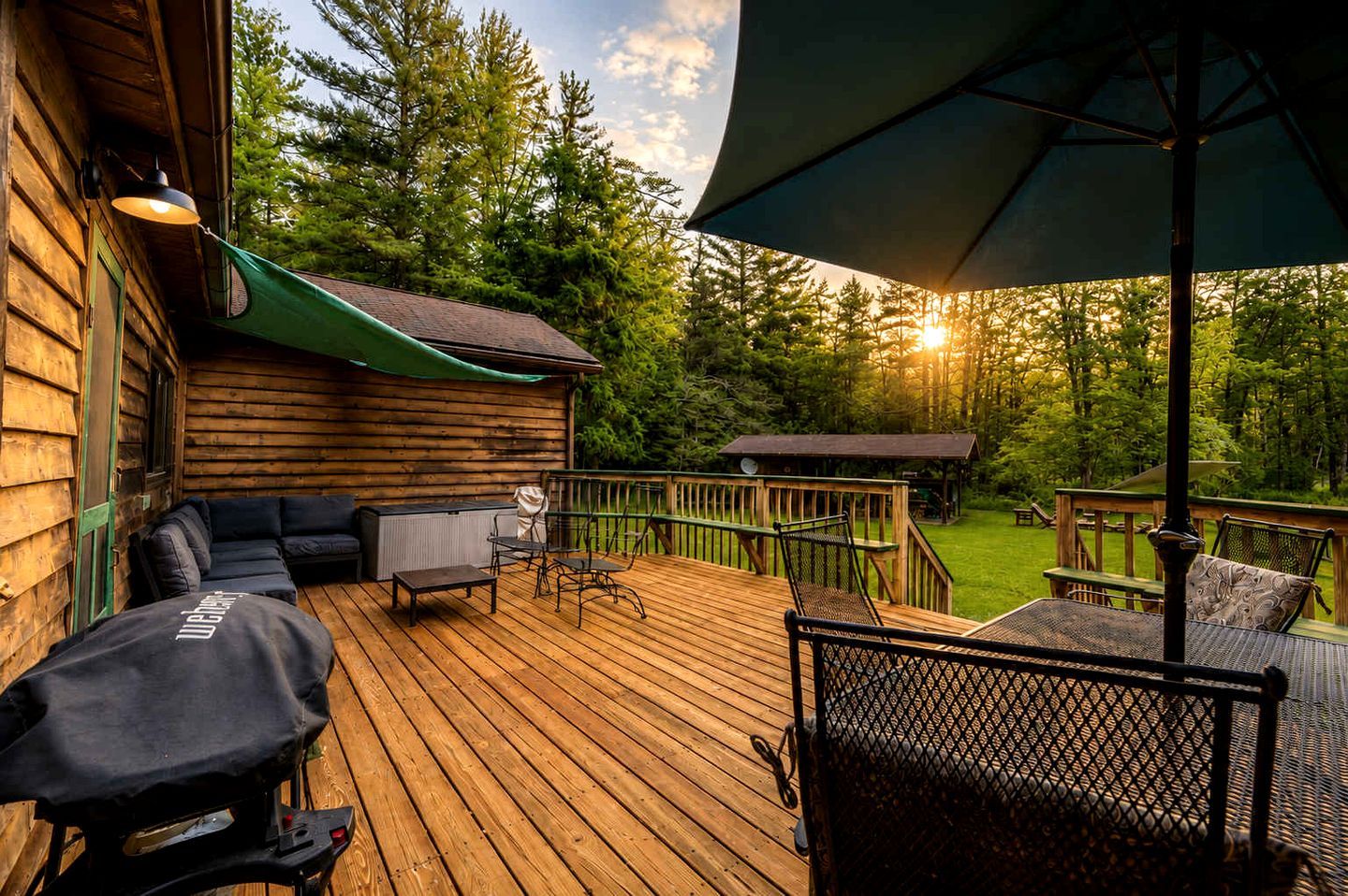 Eine Holzterrasse mit Gartenmöbeln, einem Grill und einem überdachten Bereich mit Blick auf Bäume.