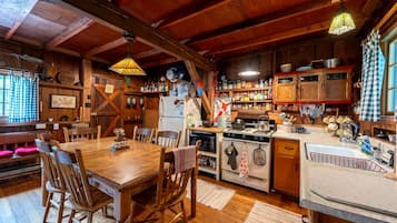 Uma cozinha rústica com vigas de madeira, uma mesa de jantar com cadeiras e diversos eletrodomésticos e utensílios.