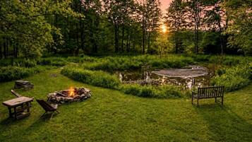 Eine friedliche Außenanlage mit einem Feuerkorb, Bänken und einem Teich, der von üppigem Grün umgeben ist.