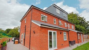 A two-story brick house with a flat roof, a large sliding glass door, and a small patio area with outdoor furniture.
