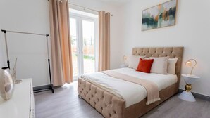 A bedroom with a large bed, a bedside table with a lamp, and a view through a glass door.
