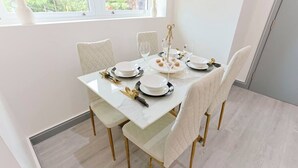 A dining table set with plates, glasses, and cutlery, surrounded by chairs with a white tablecloth.