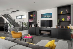 Ein modernes Wohnzimmer mit Treppe, grauen Sofas, einem gelben Sessel, einem Flachbildfernseher und einem Kamin.