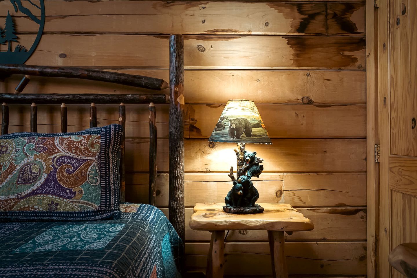 A wooden cabin interior with a bed, a lamp with a bear design, and a wall with a bear silhouette.