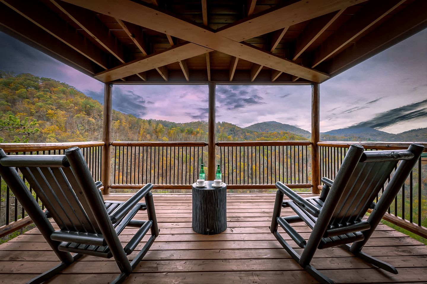 A covered deck with two rocking chairs and a small table, overlooking a mountainous landscape.