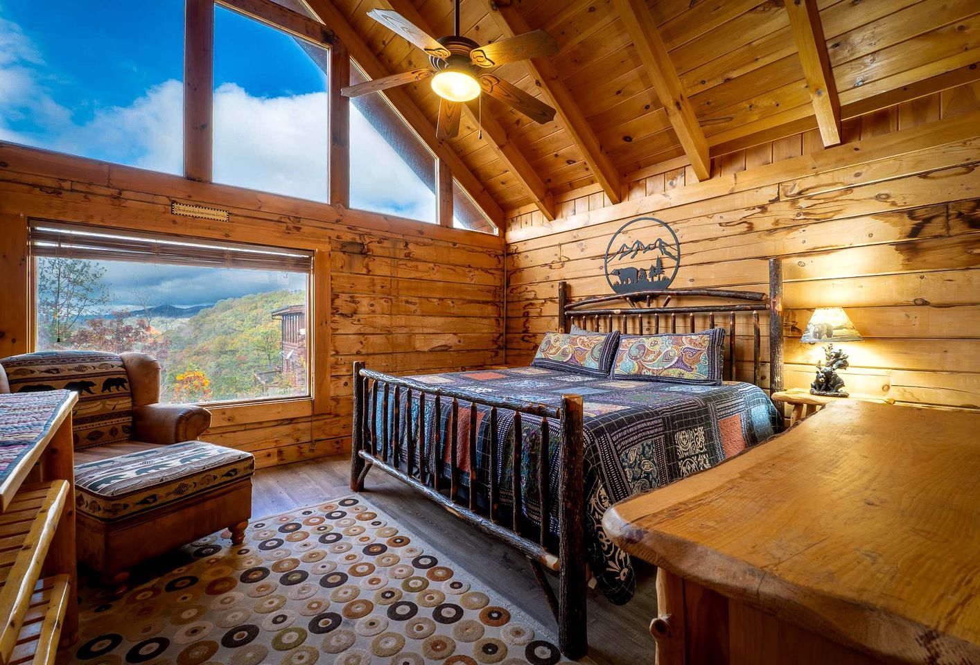 Un dormitorio de cabaña de madera con cama, una silla, una mesa y vistas a las montañas.
