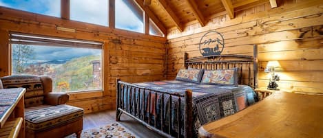 Un dormitorio de cabaña de madera con cama, una silla, una mesa y vistas a las montañas.