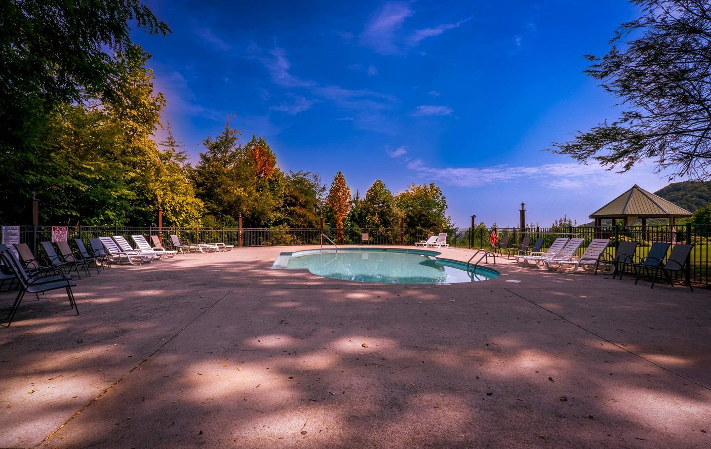 A swimming pool with lounge chairs, a gazebo, and trees in the background.