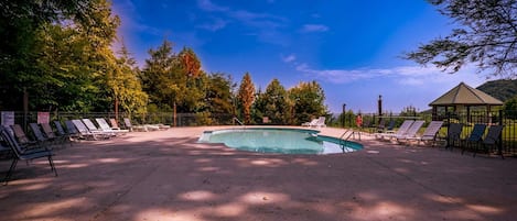 A swimming pool with lounge chairs, a gazebo, and trees in the background.