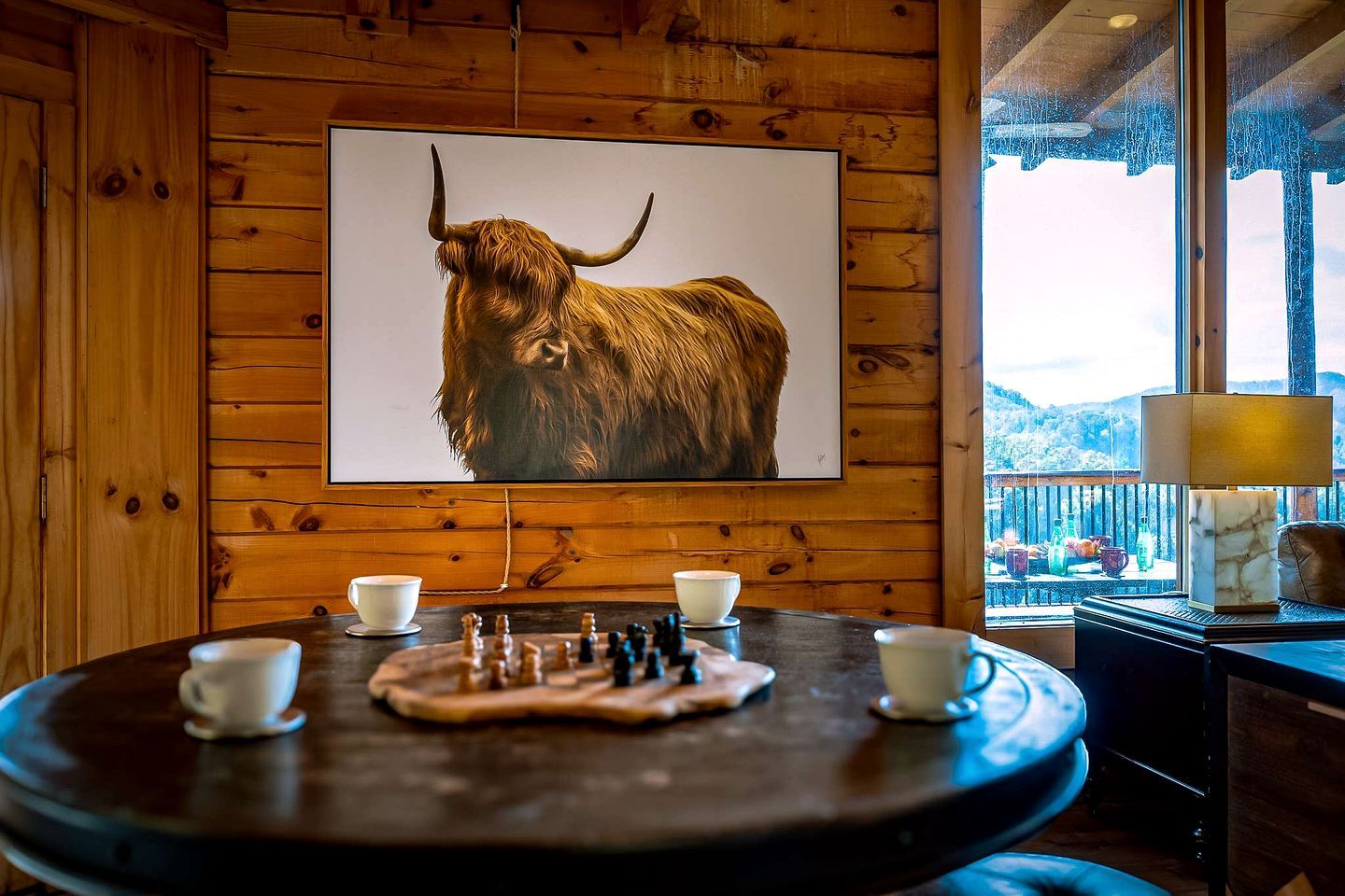 Interior de madera con un cuadro de toro montado, un tablero de ajedrez y una mesa con tazas.