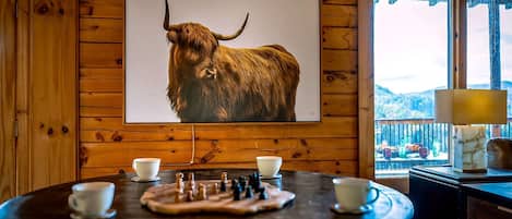 Interior de madera con un cuadro de toro montado, un tablero de ajedrez y una mesa con tazas.