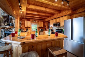 Interior d'una cabana de fusta amb cuina, que destaca una illa gran, armaris de fusta i un frigorífic d'acer inoxidable.