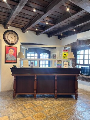 Un mostrador de recepción con un reloj, un retrato enmarcado y señales de advertencia.