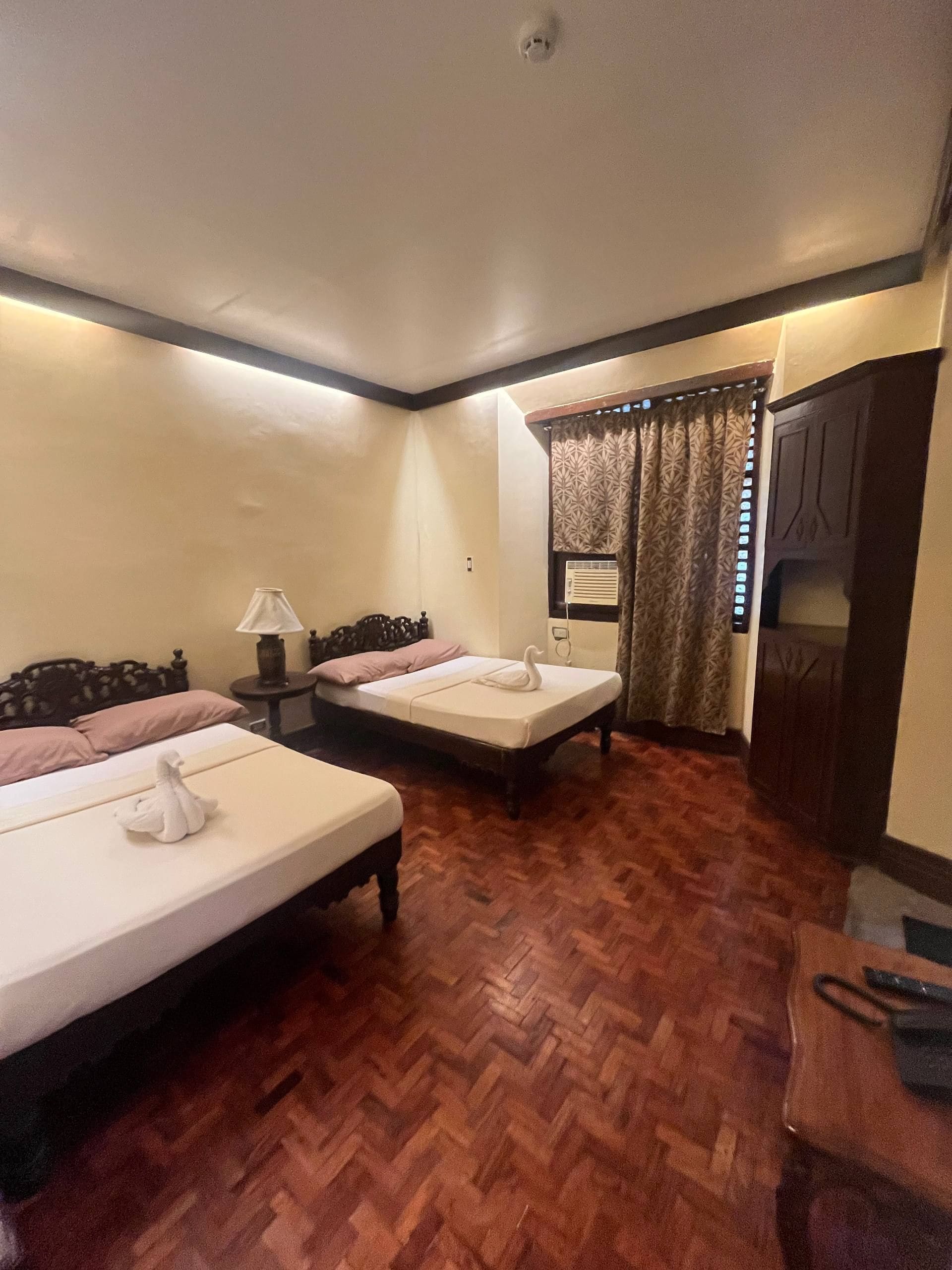 A hotel room with two beds, a wooden floor, a desk, and a wardrobe.