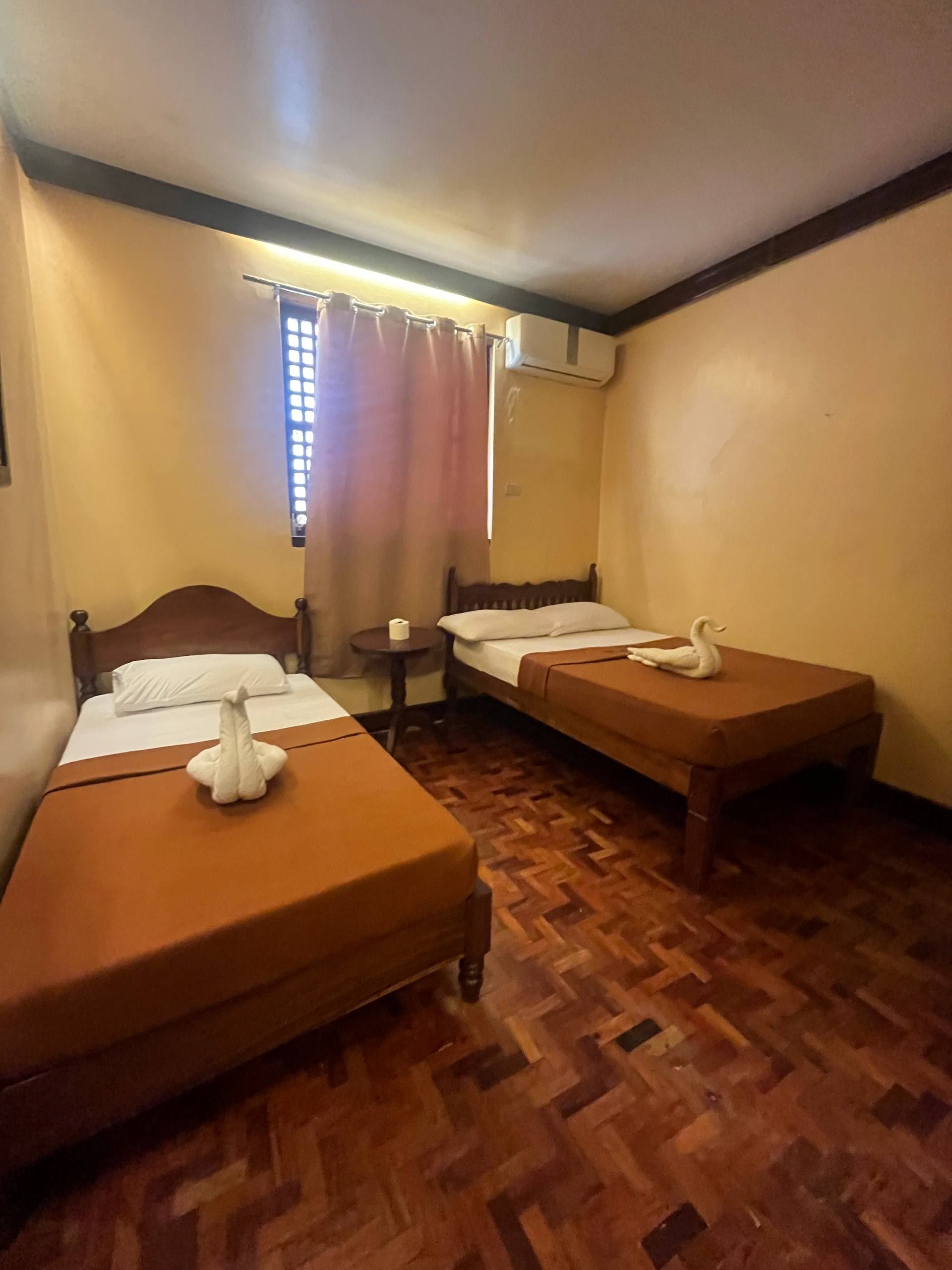 A room with two beds, a small table, and a window with curtains.