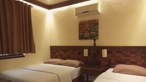 Quarto com duas camas, cabeceira de madeira, ar condicionado, um quadro e mesa de cabeceira com abajur.