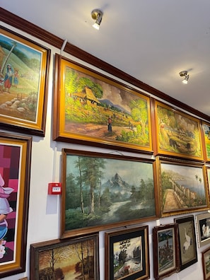 A wall with multiple framed paintings of landscapes and figures.