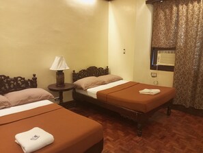 A hotel room with two single beds, a nightstand with a lamp, a window with blinds, and a wooden floor. - RF Aniceto Mansion (Vigan)