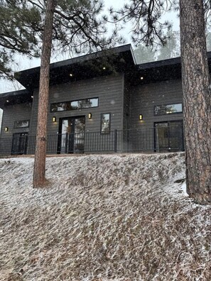 A modern building with a dark facade, large windows, and a snow-covered ground. - Radiant Family Vacation Rental Retreat near Black Hills Mountain in South Dakota (Keystone)