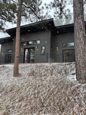 A modern building with a dark facade, large windows, and a snow-covered ground. - Radiant Family Vacation Rental Retreat near Black Hills Mountain in South Dakota (Keystone)