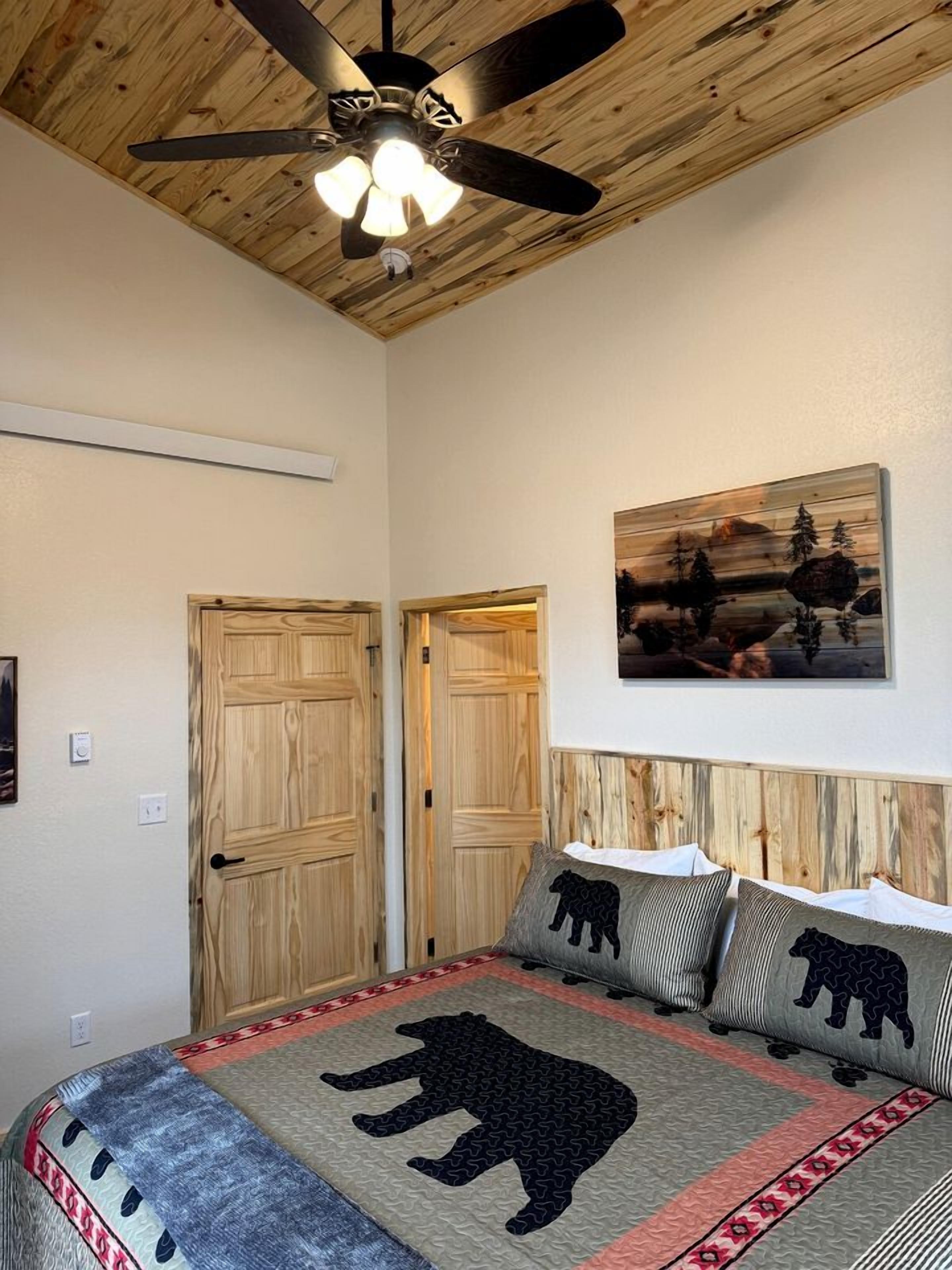 Une chambre à coucher avec un lit, deux portes en bois, un ventilateur de plafond et un tableau accroché au mur.