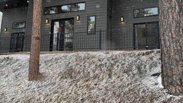 En modern byggnad med ett platt tak och stora fönster, omgiven av träd och en snötäckt mark.
