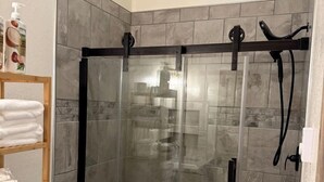 Bruseafskærmning med glasdør, toilet og hylde med sammenfoldede håndklæder.