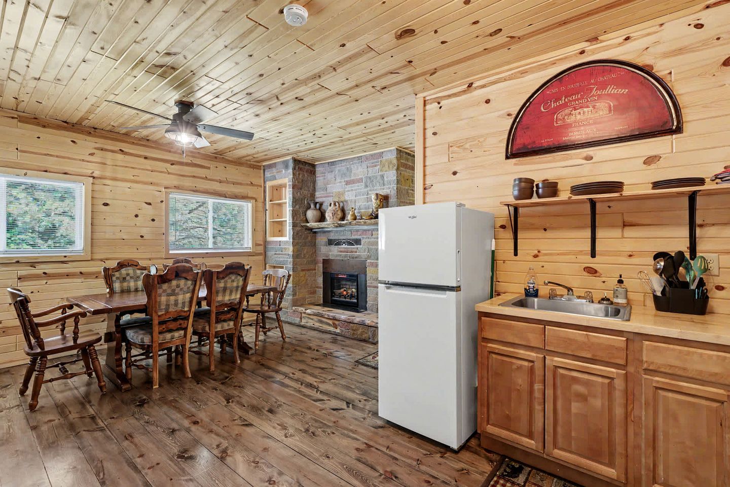 Interior de una cabaña de madera con comedor, cocina, chimenea y un letrero que indica Chateau Joulan.