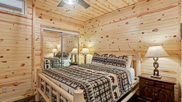 Une chambre à coucher dans un chalet en bois, avec un lit, deux tables de chevet avec des lampes, un ventilateur de plafond et un grand miroir.