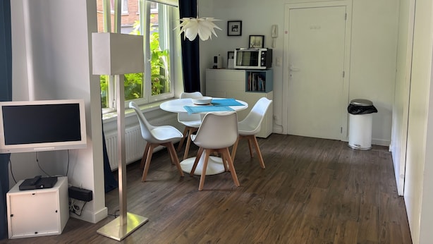 A modern kitchen with white appliances, a dining table with chairs, and a large window with curtains.