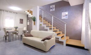 Ein modernes Wohnzimmer mit einer Couch, einem Esstisch, Stühlen, einer Treppe und einer Pflanze.