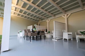 Eine überdachte Terrasse im Freien mit Esstisch, Stühlen und Topfpflanzen.