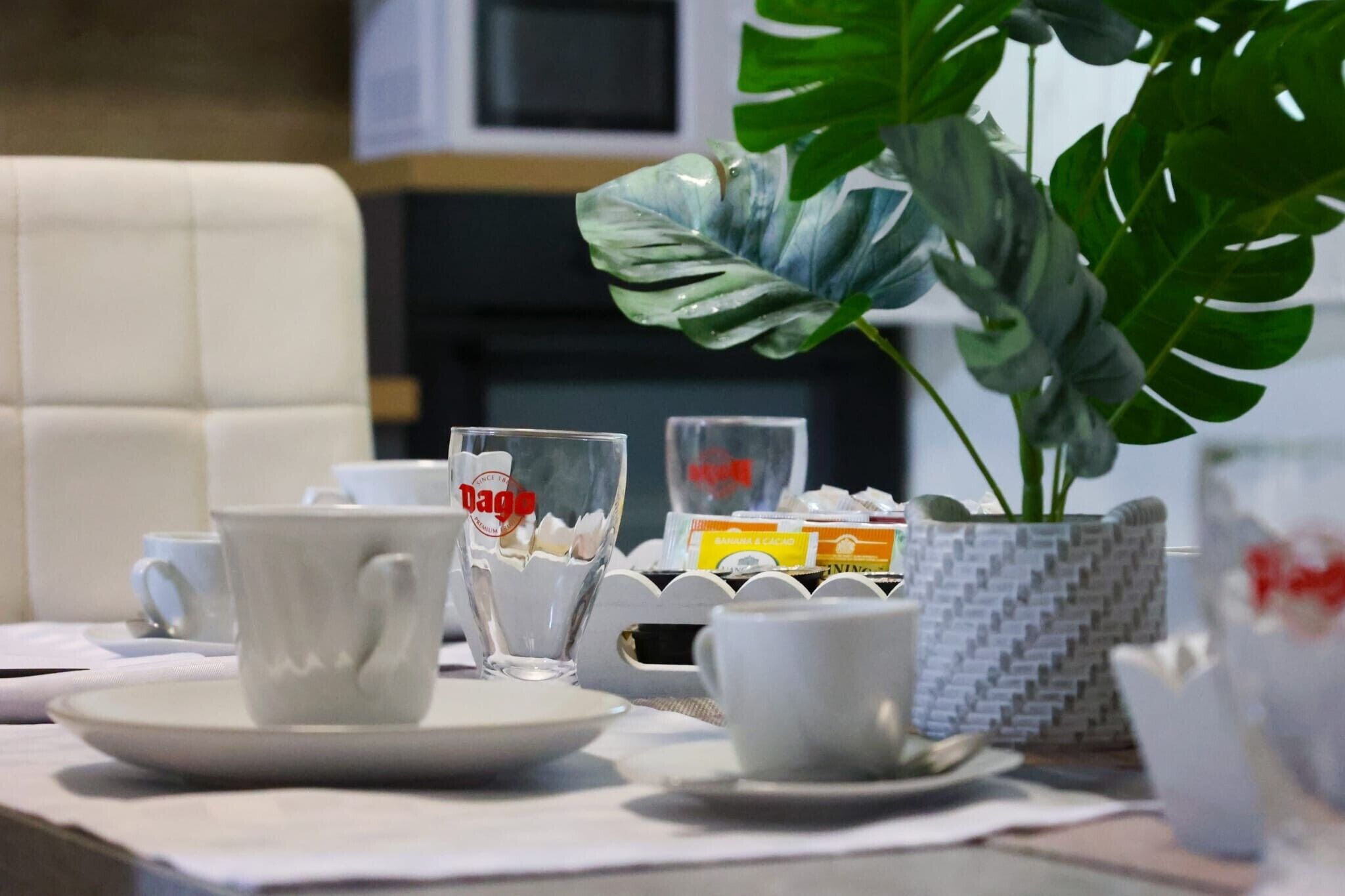 A table with a white cup, a glass, and a plant in a patterned pot.