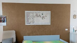 Una habitación con un sofá azul, una pequeña mesa redonda con una tableta, una obra de arte enmarcada en la pared y una silla negra.