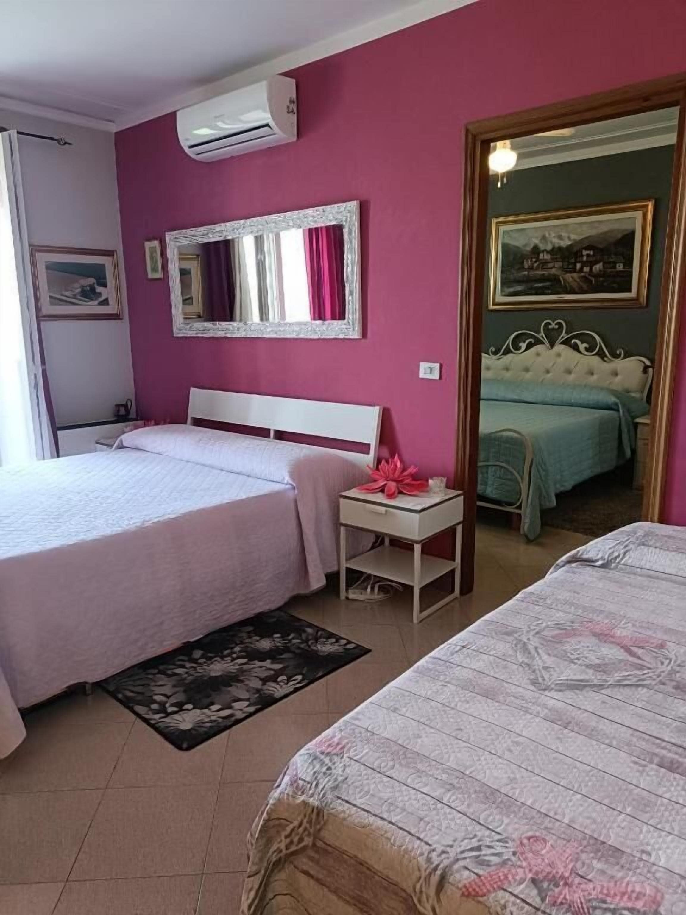 Quarto com duas camas, uma mesinha de cabeceira, um espelho e uma porta que dá para outro cômodo.