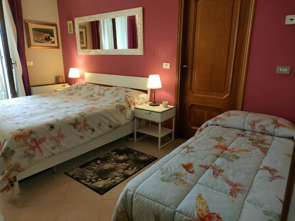 Una habitación de hotel con dos camas, un espejo, una mesita de noche con lámpara y una puerta.