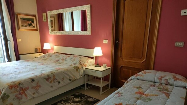 Una habitación de hotel con dos camas, un espejo, una mesita de noche con lámpara y una puerta.