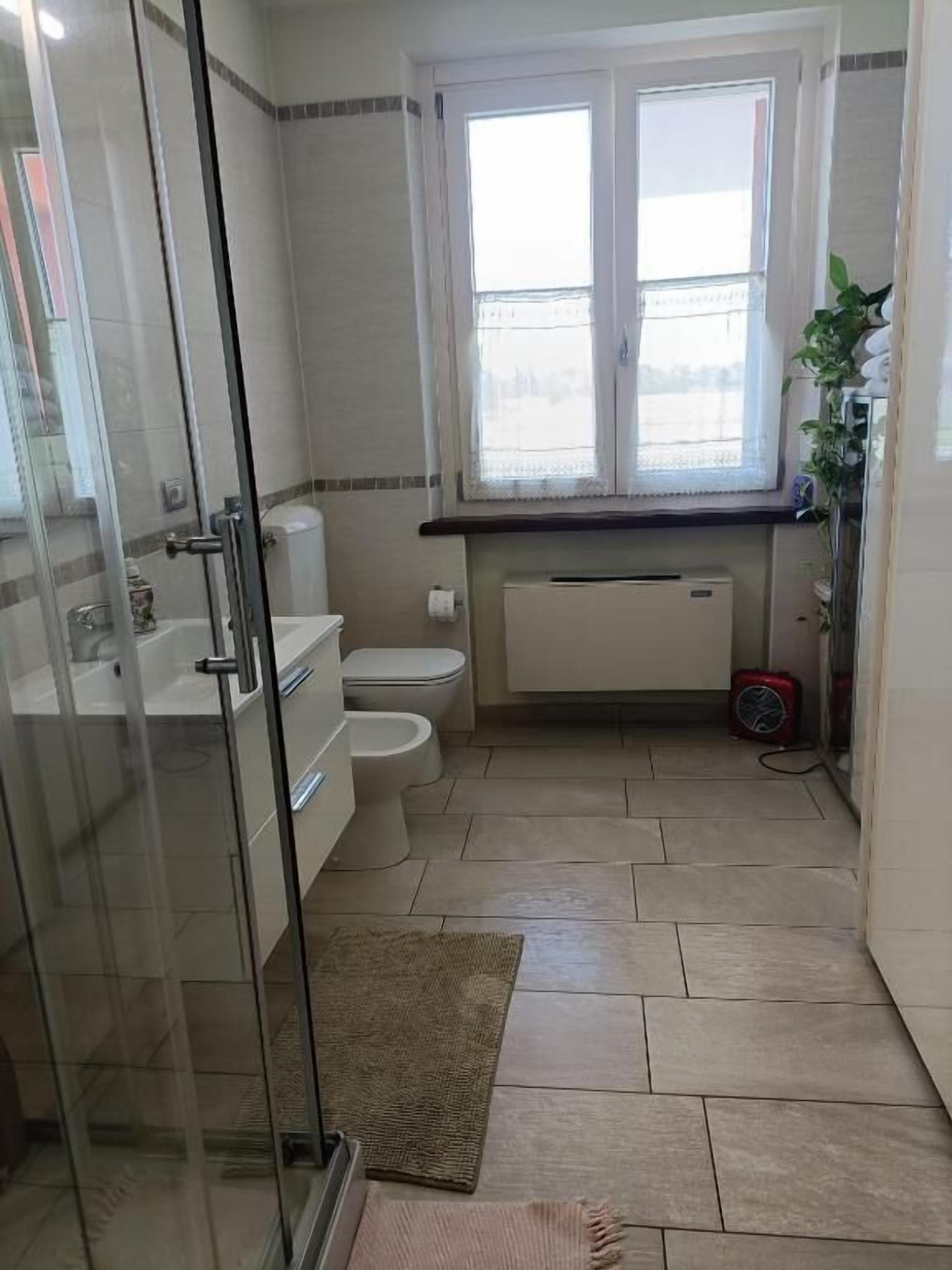 Un baño con cabina de ducha de vidrio, inodoro, lavamanos y ventana.