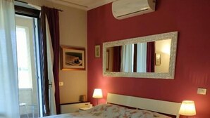 Hotellihuone, jossa on sänky, kaksi yöpöytää, peili, ikkuna verhoilla ja seepramustalla kuviolla koristeltu matto.