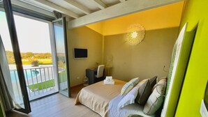 A bedroom with a bed, a small table, a chair, a TV, and a balcony with a view. - Masseria Sant'Eleuterio (Collepasso)