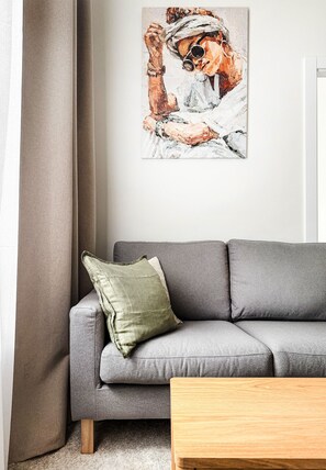 A grey sofa with a green pillow and a wooden coffee table in a living room with a painting on the wall. - Premium Apartment with A/C, city center Cracow, Dąbrowskiego (Kraków)