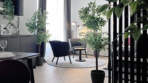 Ett modernt vardagsrum med en matplats, en svart soffa, ett runt bord och två krukväxter.