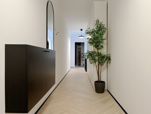 Un couloir avec une armoire sombre, une plante en pot et un luminaire suspendu.
