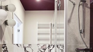 Een badkamer met een marmeren wastafel, een douche en een douchecabine met glazen wanden.
