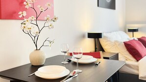 Een eethoek met een gedekte tafel voor twee personen, een vaas met bloemen, en een modern abstract schilderij aan de muur.
