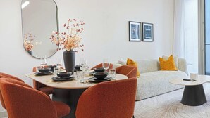 Een moderne woonkamer met een bank, een salontafel en een eethoek met stoelen en een tafel voor vier personen.