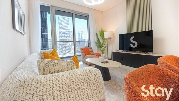 Een moderne woonkamer met een bank, een voetenbankje, een salontafel en een flatscreen televisie.