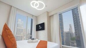 Een hotelkamer met een groot bed, uitzicht op stadsgebouwen en een bord met de letter 'S' aan de muur.